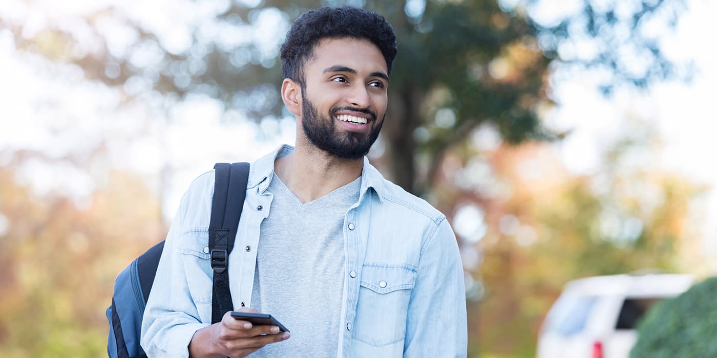 A college student wearing a backpack while using a smartphone.