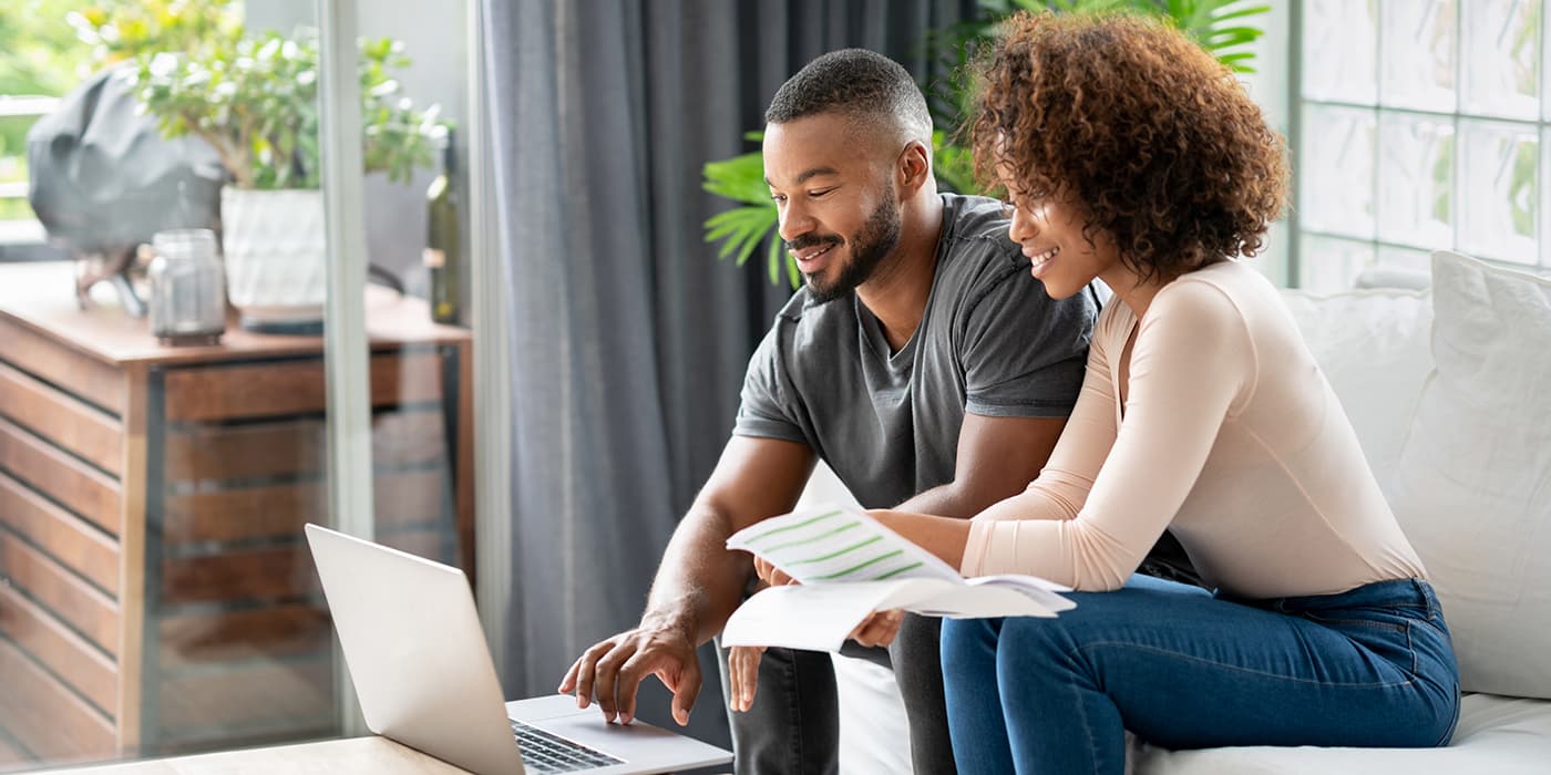 A young couple sitting on a couch and using a laptop to pay bills.