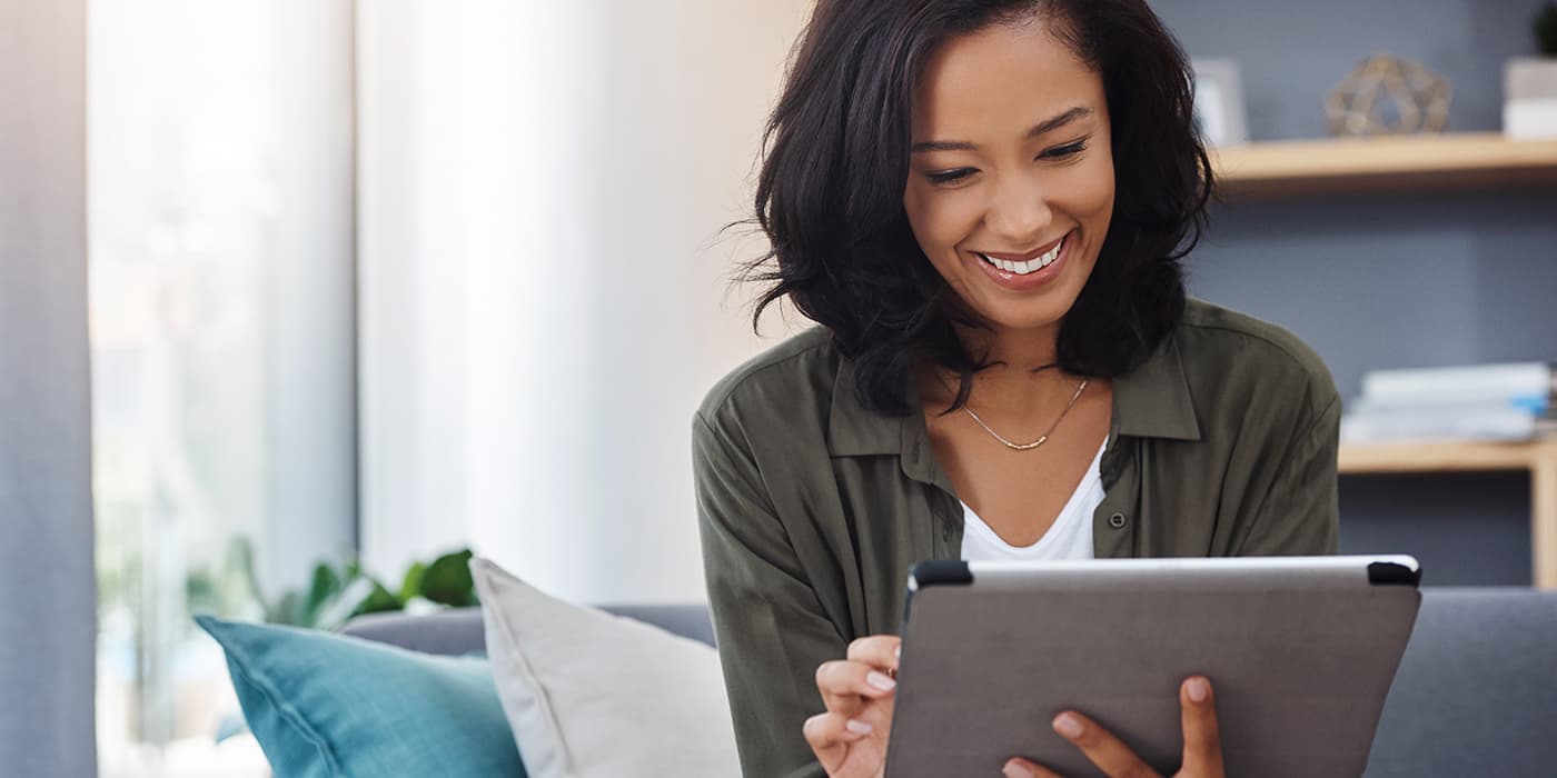 A middle-aged woman sitting on a couch while using a tablet.