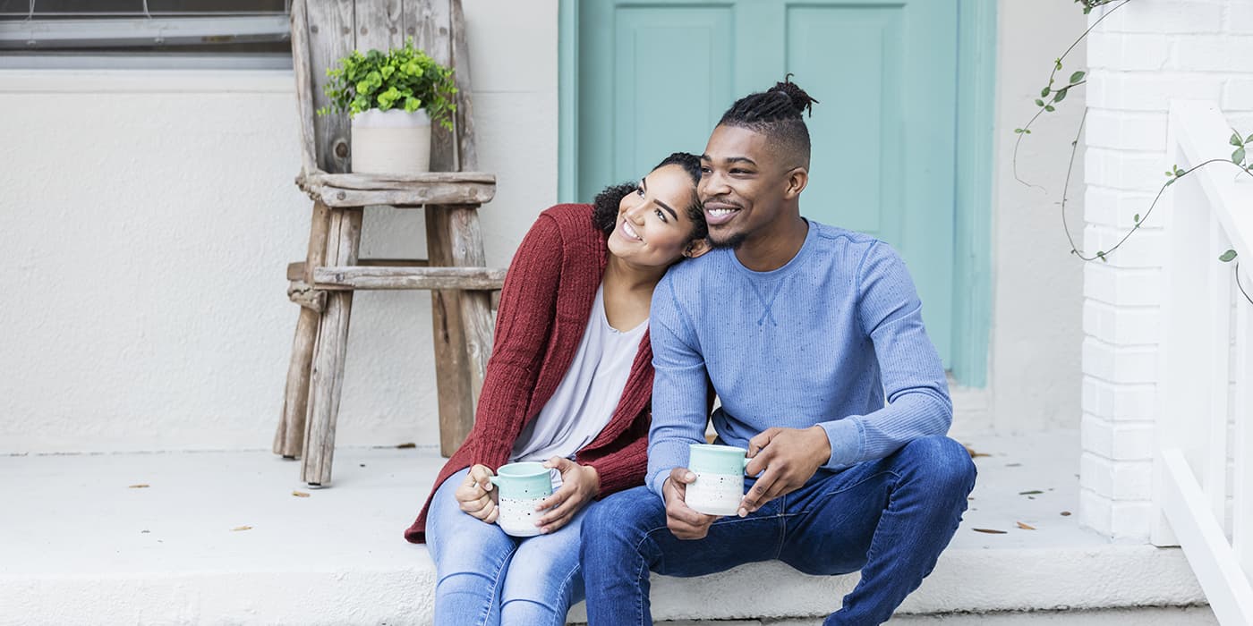 A young couple sitting on their porch drinking coffee.