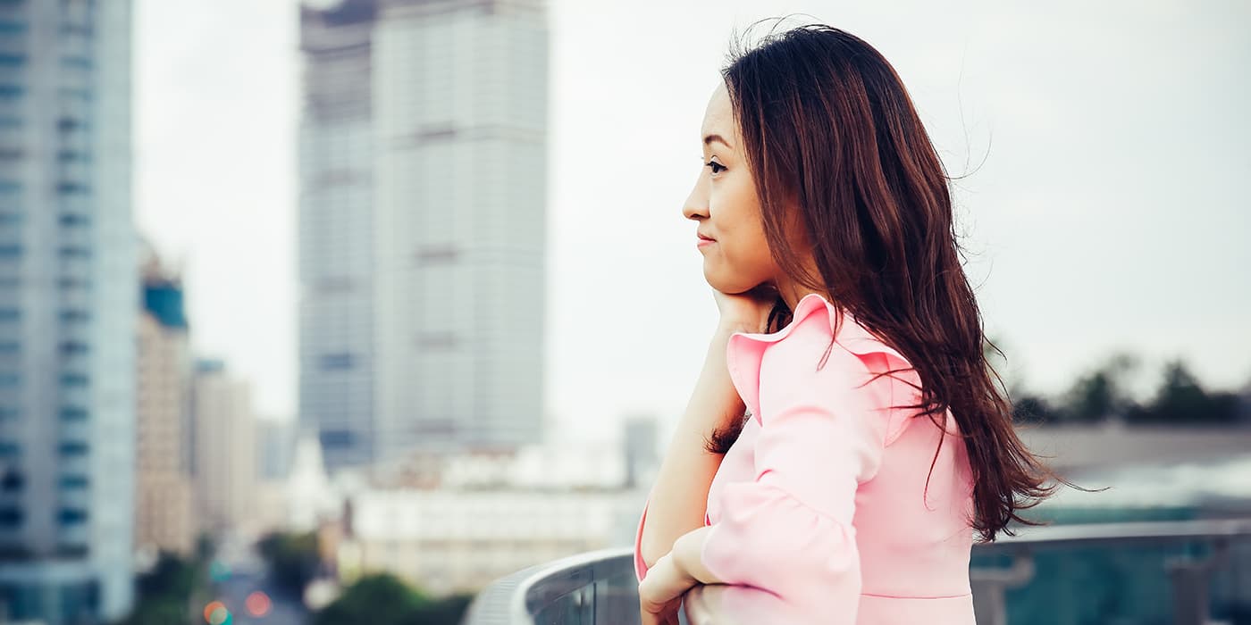 A young woman standing on a balcony overlooking a city skyline.